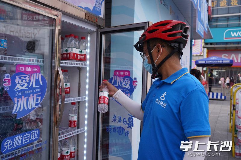 7月20日，一名快送骑手在天心区黄兴路步行街中心广场的爱心冰柜站点自取免费的矿泉水。